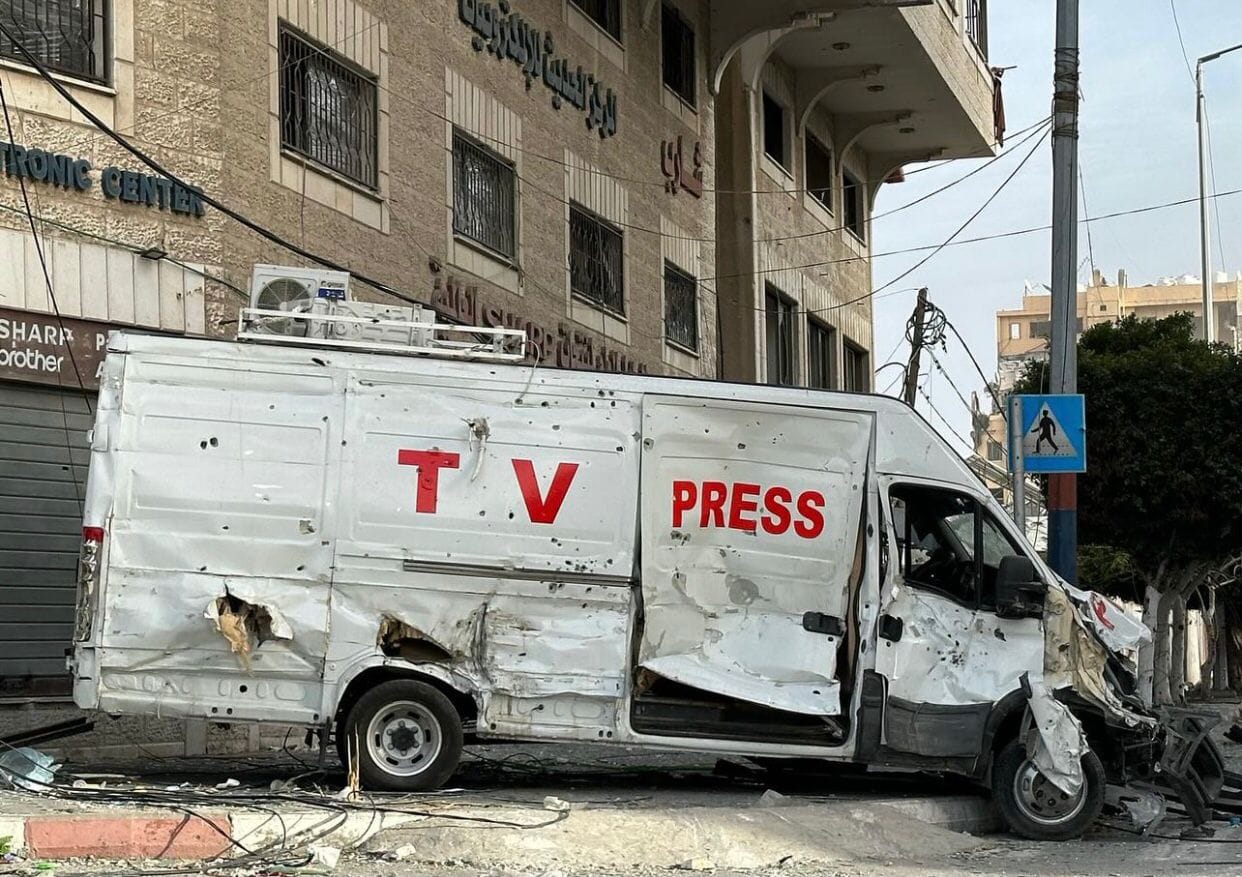 A white van with the words "TV PRESS" is pictured, heavily damaged. There are bullet holes on the side and the front is smashed.