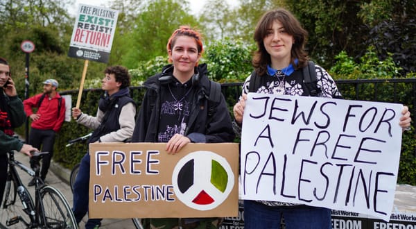 Two protesters holding signs saying "Jews for a free Palestine" and "Free Palestine" with a peace sign in Palestinian colours