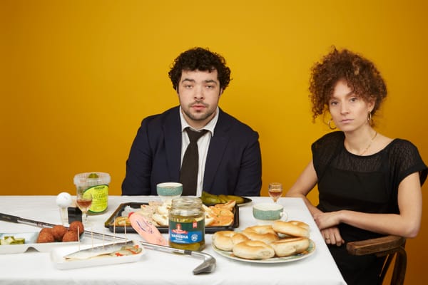 Dylan Corbett-Bader and Gemma Barnett sit next to each other at a dining table covered in traditional Jewish foods.