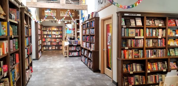 Interior of a bookshop with grey floors, dark wood bookshelves and rainbow bunting