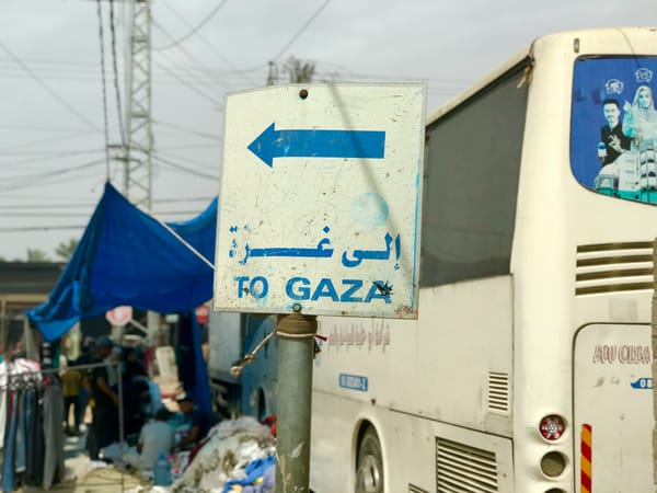 A blue-and-white sign reads "To Gaza" next to a parked white bus.