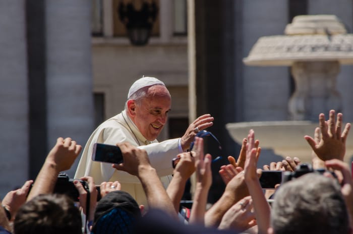 Among the grandeur of the Vatican, a pope intimately greets a gathering of people. Credit: Alfredo Borba